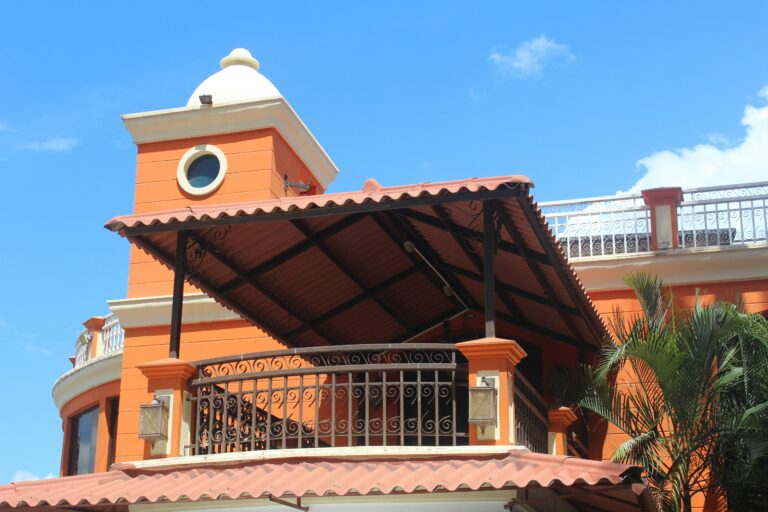 A striking orange house exterior featuring a metal balcony and unique architectural design.