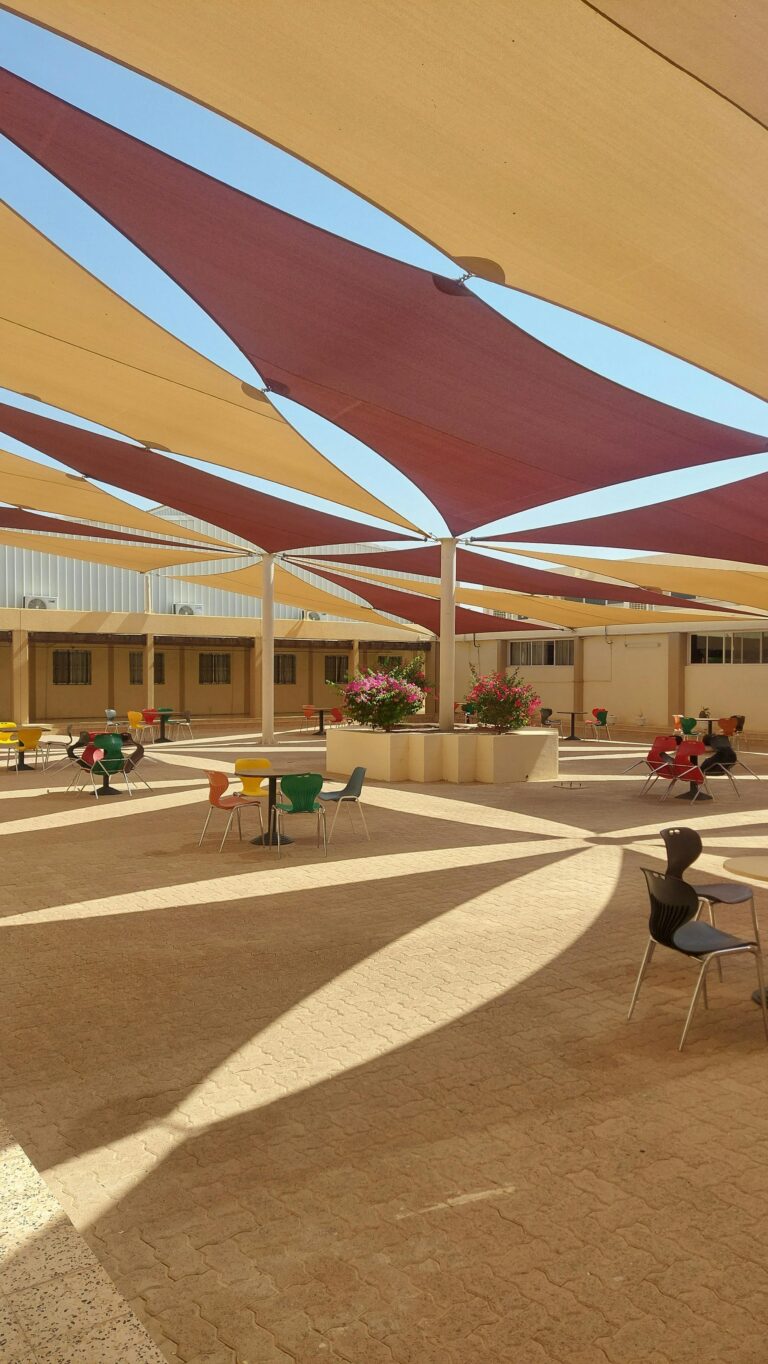 A vibrant outdoor seating area with colorful chairs and geometric sunshades casting shadows.