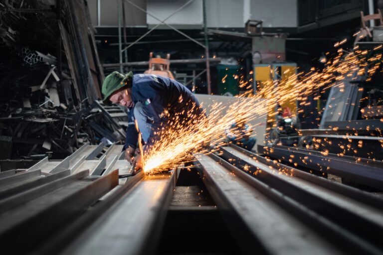 A worker uses an angle grinder, creating sparks in a metal workshop.