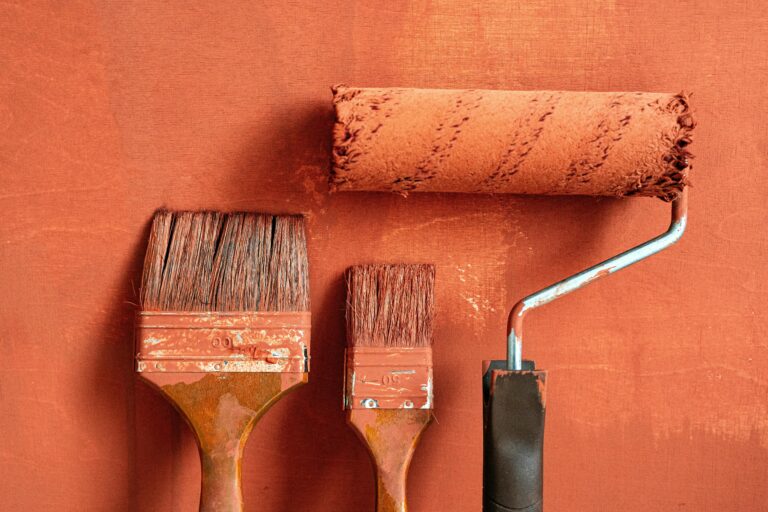 Painting tools including two brushes and a roller on an orange painted surface.