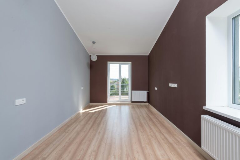 Spacious empty room featuring wooden flooring and a large window with natural light.