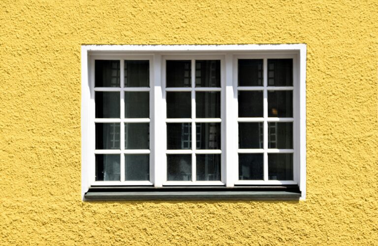 A vibrant yellow textured wall with a classic white framed window in Prien am Chiemsee, Germany.